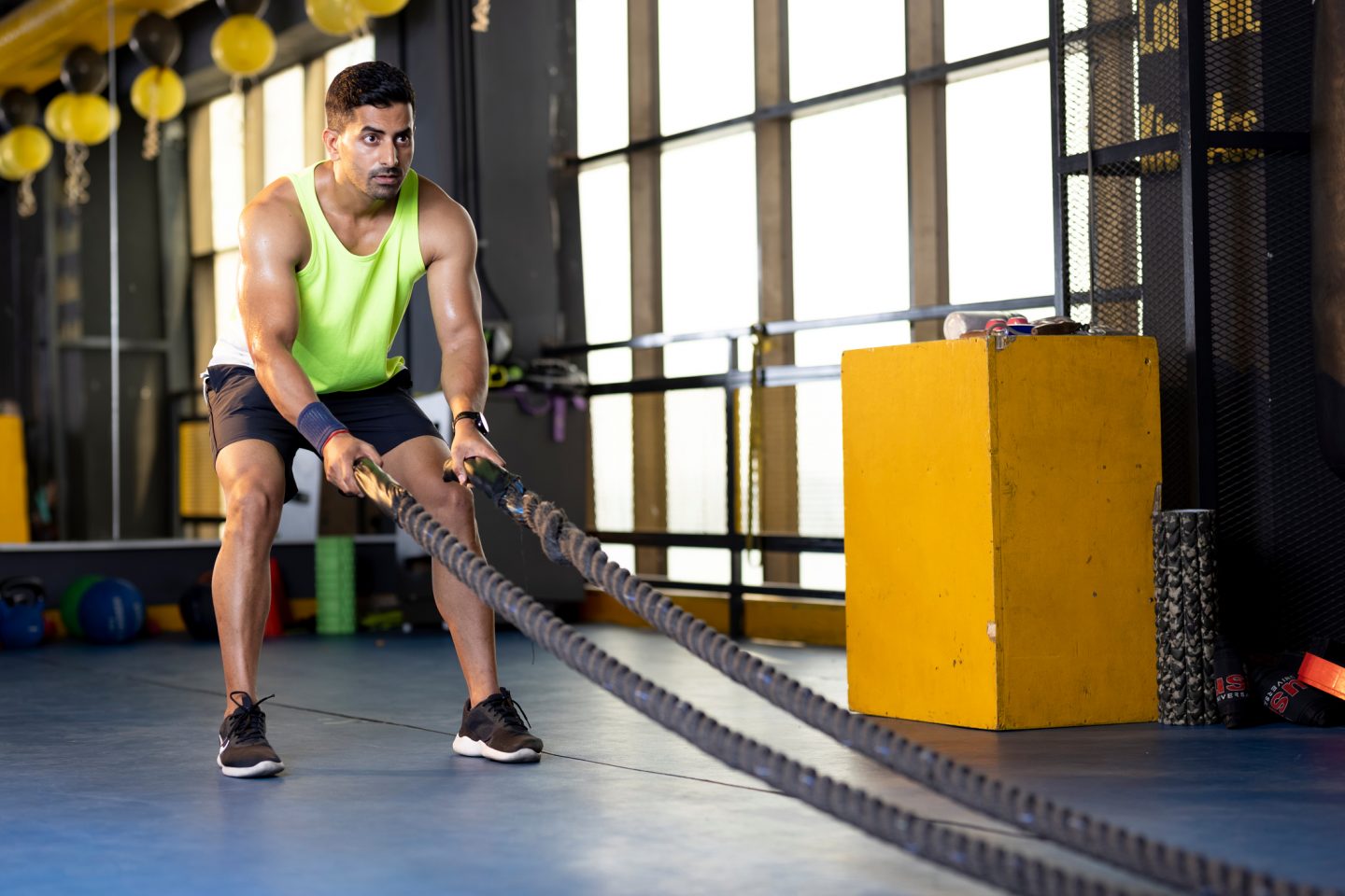 Active old man in sportswear training with battle rope in gym gym