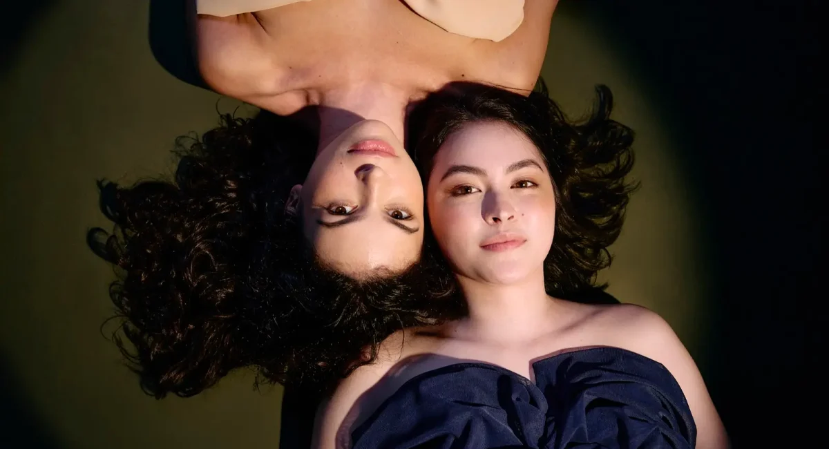 Foto de divulgação de "Antígona". Fernanda Gidali e Julia Gaspar estão deitadas no chão, olhando diretamente para a câmera