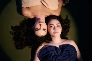Foto de divulgação de "Antígona". Fernanda Gidali e Julia Gaspar estão deitadas no chão, olhando diretamente para a câmera