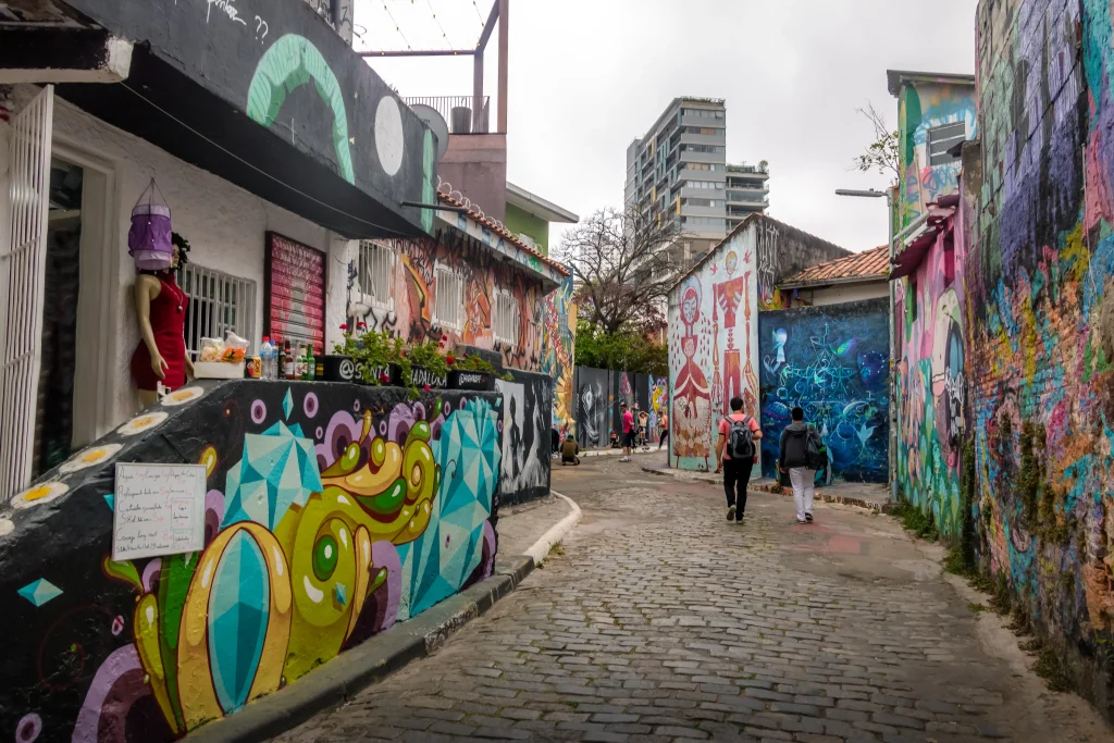 Beco do Batman. Uma viela de paralelepípedo cercada de muros de casinhas. Os muros possuem diversos grafites coloridos