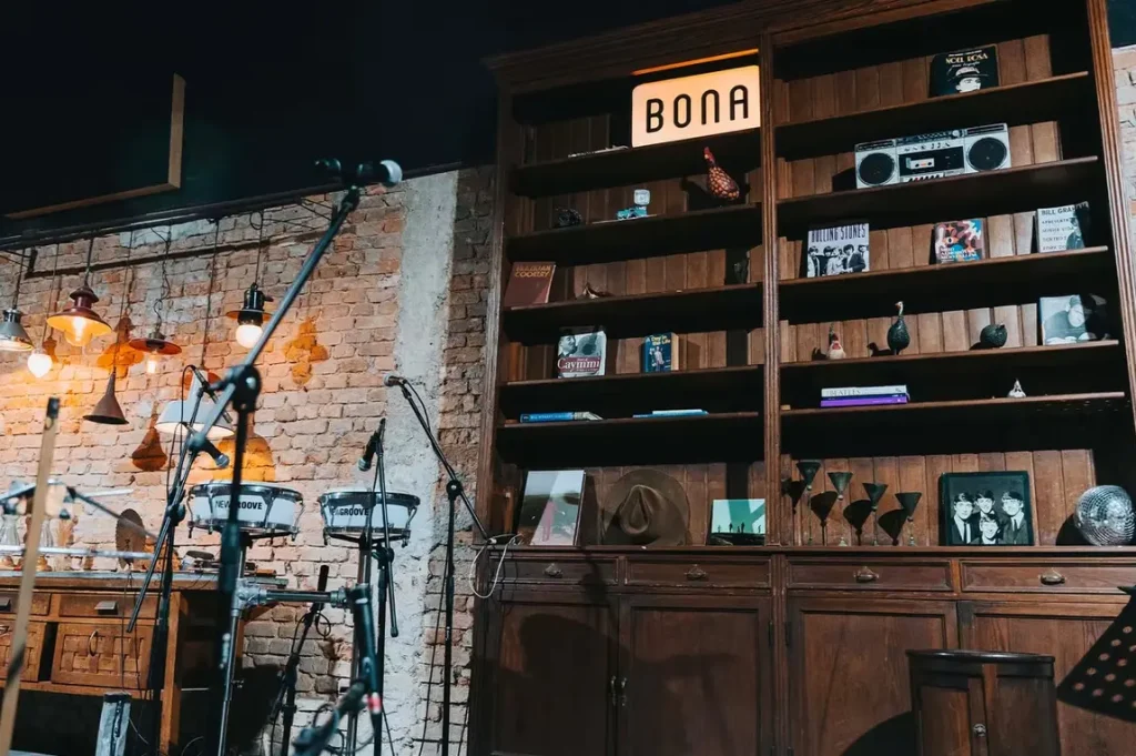 Palco da Bona Casa de Música. O fundo é composto por uma parede de tijolos e uma estante de madeira recheada de objetos