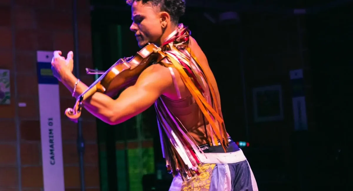 O multiartista Mafê em "Encantaria Brincante". Ele toca seu violino durante a apresentação. Veste um figurino composto por diversas fitinhas e retalhos coloridos