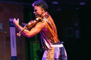 O multiartista Mafê em "Encantaria Brincante". Ele toca seu violino durante a apresentação. Veste um figurino composto por diversas fitinhas e retalhos coloridos