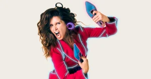 Foto de divulgação de "Imagina na Adolescência". Priscila Assum está pulando; descalsa, ela segura um salto azul na mão; veste um terninho vermelho e calça roxa; sua silhueta é contornada por neons azuis