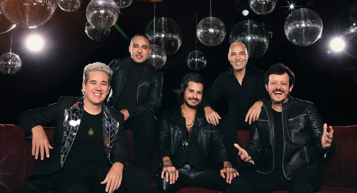 O grupo Jota Quest posa em um sofá preto. Ao fundo, diversos globos espelhados