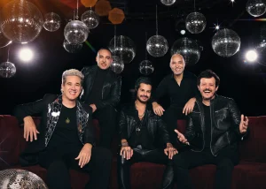 O grupo Jota Quest posa em um sofá preto. Ao fundo, diversos globos espelhados