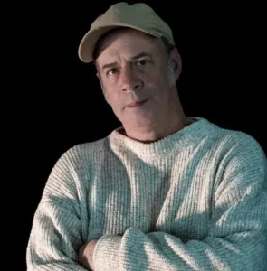 O cantor e compositor Junio Barreto. Ele está de braços cruzados, vestindo um sueter e boné cinzas