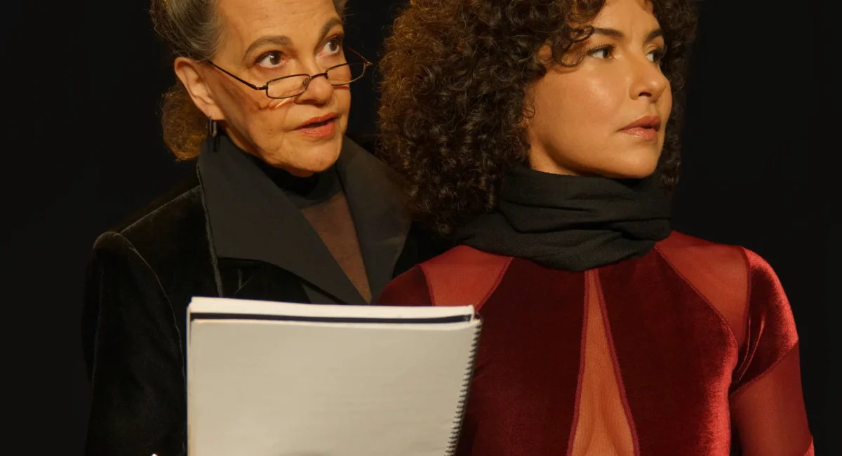Foto de divulgação de "Sopro". Noemi Marinho, à esquerda, segura o texto de uma peça e o dita no ouvido da atriz Amanda Acosta