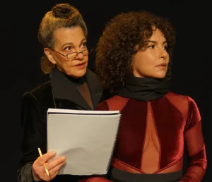 Foto de divulgação de "Sopro". Noemi Marinho, à esquerda, segura o texto de uma peça e o dita no ouvido da atriz Amanda Acosta